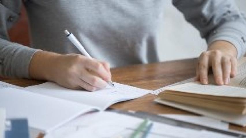 Una persona tomas notas en un cuaderno mientras hojea un libro