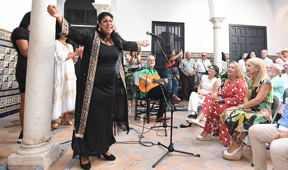 Cantaora de flamenco durante una actuación, acompañada de guitarrista y palmeras