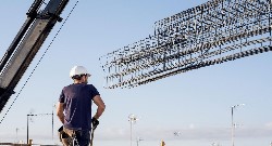 Un trabajador maneja una grúa que transporta un gran cantidad de forjado de hierro